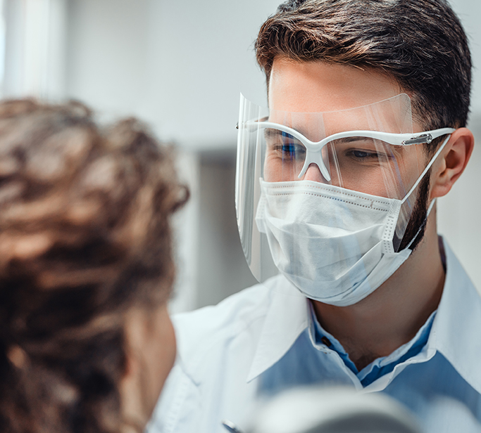 Smiling male healthcare worker wearing safety glasses, face shield and mask while treating patient